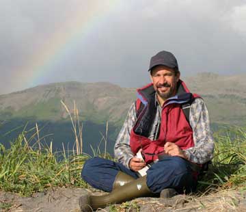 Dr. P sitting on ground with rainbow in the background.